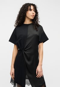 Μαύρο φόρεμα με κοντά μανίκια, με λεπτομέρεια στριφώματος στη μέση και δαντελένιο τελείωμα, που συνδυάζει ματ και διάφανα υφάσματα.