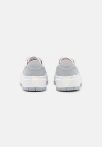 Graue und weiße Sneakers mit einer klobigen Sohle, glattem Leder- und Textilobermaterial, gepolstertem Kragen und dezentem Logo auf der Rückseite.