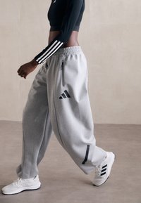Pantaloni grigi in felpa con zip laterali e dettagli neri. Abbinati a un crop top nero a maniche lunghe e sneakers bianche con strisce nere.