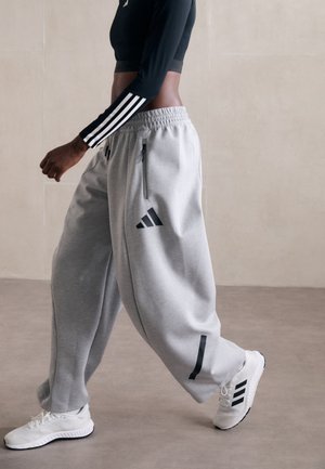 Pantalons de survêtement gris avec des zips sur le côté et des accents noirs. Associés à un crop top noir à manches longues et des baskets blanches avec des rayures noires.