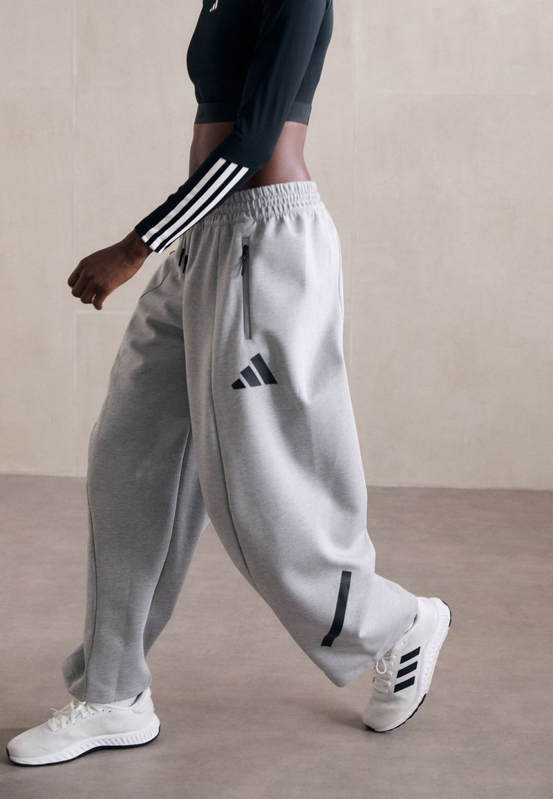 Pantaloni grigi in felpa con zip laterali e dettagli neri. Abbinati a un crop top nero a maniche lunghe e sneakers bianche con strisce nere.