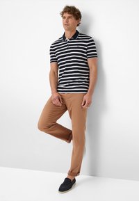 Navy and white striped polo shirt with a collar, paired with tan chinos and navy slip-on shoes, set against a plain white background.