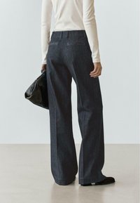 Jeans di denim scuro a gamba larga con vita alta, orli rifiniti e due tasche posteriori. Abbinati a un top bianco aderente a maniche lunghe e una borsa nera.