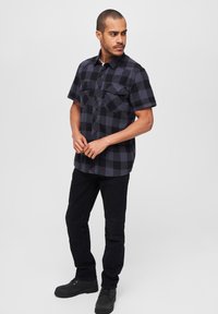 Zwart en grijs geruit overhemd met korte mouwen en twee borstzakken, gecombineerd met zwarte jeans en zwarte laarzen. Glad materiaal met een knopenkraag.