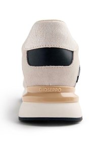 Sneaker crema con tomaia testurizzata, accentuazione nera nel tallone, suola beige e logo impresso sul retro. Presenta un design elegante e moderno.