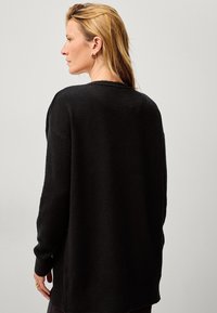Zwarte gebreide trui met een losse pasvorm, lange mouwen en een ronde halslijn. Zachte textuur, minimalistisch ontwerp en geen zichtbare patronen of accenten.