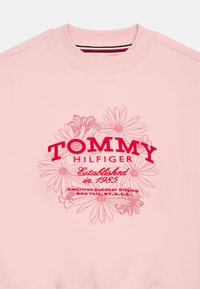 Φωτεινό ροζ φούτερ με ραμμένο λαιμό. Διαθέτει γραφικό σχέδιο με λουλούδια και κόκκινο κείμενο "TOMMY HILFIGER", με την ένδειξη "Ιδρύθηκε το 1985".