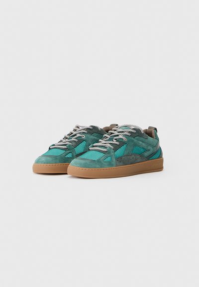 Grønne og sjøgrønne sneakers med en blanding av semsket skinn og nettmaterialer, runde lisser og en tan gummisåle. Detaljer inkluderer utskårne designelementer.