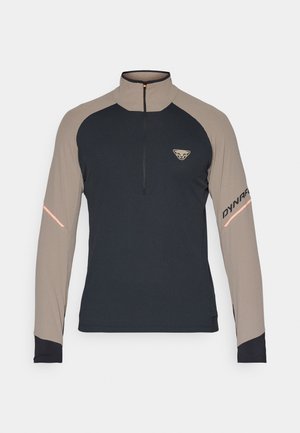 Langærmet skjorte med kvart lynlås i marineblå og beige. Har struktureret stof og reflekterende detaljer på ærmerne. Logo på brystet.