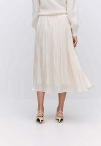 Plisségedeelte crèmekleurige midi-rok met een vloeiende uitstraling, lichte stof, elastische taille en een zacht vallende silhouet. Draag met lichtgekleurde hakken.