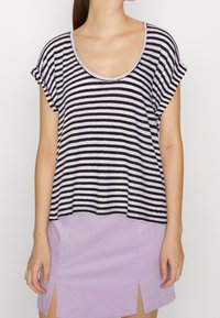 Pruhované tričko s krátkým rukávem v námořnické modři a bílé, s kulatým výstřihem a volným střihem, v kombinaci s lehkou levandulovou sukní s rozparky.