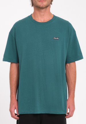 T-shirt en coton teal avec une coupe décontractée et des manches courtes. Présente une petite étiquette noire avec "Volcom" sur la zone de la poitrine gauche.