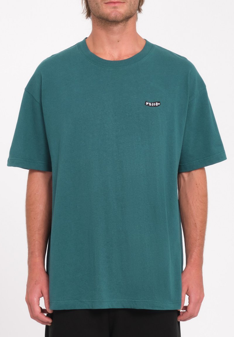 T-shirt in cotone teal con una vestibilità rilassata e maniche corte. Presenta un piccolo etichetta nera con la scritta "Volcom" nella zona sinistra del petto.