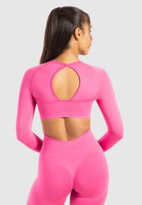 Vrouw in een felroze lange mouw sporttop en bijpassende hoog-taille leggings, die haar rug toont met een sleutelgatuitsnijding op de top.