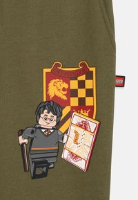 Λαδί ύφασμα με το έμβλημα του Γκρίφιντορ, φιγούρα LEGO του Χάρι Πότερ κρατώντας τον Χάρτη των Μάραuders, διακοσμημένο με κόκκινες και κίτρινες λεπτομέρειες.