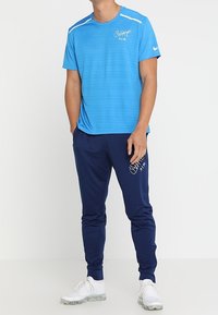 Blauwe sportt-shirt met horizontale strepen en Nike-logo, gecombineerd met navy joggers met een logo, en witte sportschoenen.