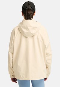 Beige waterdichte jas met een capuchon, elastische manchetten en een relaxte pasvorm. De achterkant heeft een gladde textuur en minimale details.