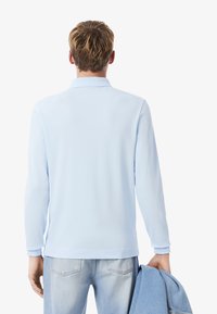 Pitkähihaista polo-paitaa vaaleansinisestä kankaasta, jossa on kaulus ja ribattu hihansuu, yhdistettynä vaaleansinihin farkkuihin, jotka on yhdistetty samaan sävyyn takkiin.