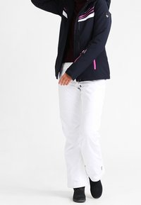 Tmavě modrá zimní bunda se bílými a růžovými pruhy, zapínáním na zip vpředu a kapucí. Doplněna bílými sněhovými kalhotami a černými botami.