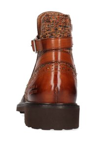 Botín de cuero marrón hasta el tobillo, con parte superior de tela texturizada, detalle de hebilla y perforaciones decorativas en los laterales, con una suela de goma resistente.