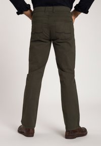Pantalones verde oliva oscuro con piernas rectas, bolsillos traseros visibles y detalles de costura en contraste, combinados con zapatos marrones.