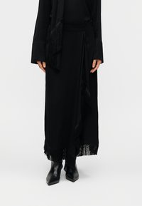 Μαύρο μακρύ φόρεμα με φούντες στο τελείωμα και στις πλευρές, κατασκευασμένο από απαλό ύφασμα. Συνδυασμένο με μαύρα μυτερά μποτάκια έως τον αστράγαλο και μακριά μανίκια.