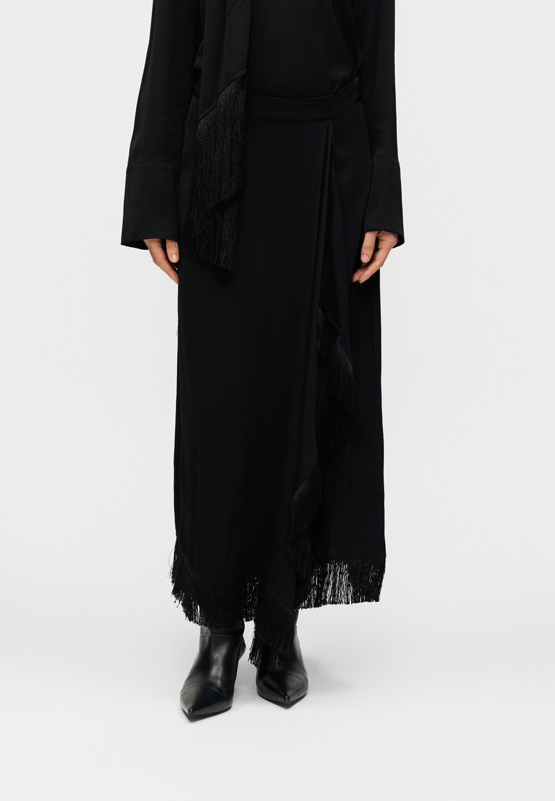 Μαύρο μακρύ φόρεμα με φούντες στο τελείωμα και στις πλευρές, κατασκευασμένο από απαλό ύφασμα. Συνδυασμένο με μαύρα μυτερά μποτάκια έως τον αστράγαλο και μακριά μανίκια.