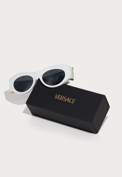 Valged üleolevad päikeseprillid tumedate läätsedega, millel on kuldsed aksessuaarid. Karp on must, millel on kuldsete tähtedega "VERSACE".