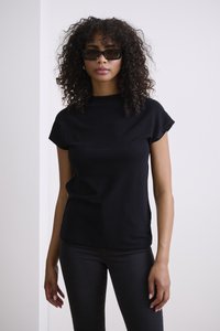 Haut noir à manches courtes avec un col montant, associé à un jean noir moulant. Le tissu semble lisse avec une texture subtile.
