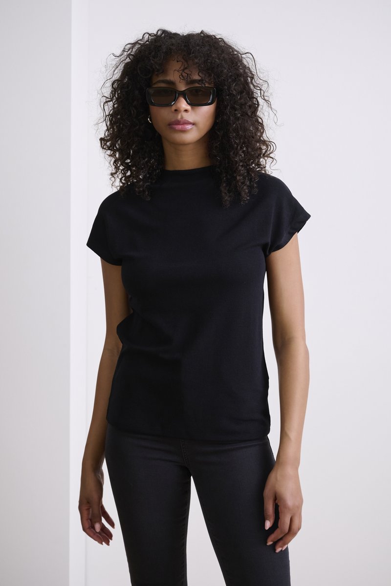 Haut noir à manches courtes avec un col montant, associé à un jean noir moulant. Le tissu semble lisse avec une texture subtile.