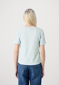 Svetlou modrá blůza s krátkým rukávem s texturovaným diamantovým vzorem a detaily z perliček. Kulatý výstřih, mírně volný střih a měkká tkanina.