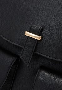 Czarna skórzana torebka o fakturowanym wykończeniu, wyposażona w złocony metalowy zatrzask i klapę zapinaną na zatrzask. Gładkie skórzane elementy i detale w postaci przeszyć.