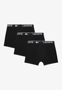Čierne bavlnené boxerky v trojbalení, s bielym elastickým pásom s logom "LACOSTE" a emblémom krokodíla. Hladká textúra.