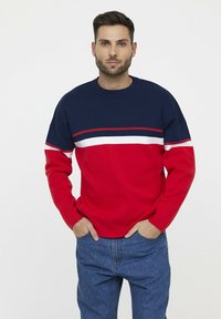 Pull rouge et marine à col rond, avec une accent rayé blanc et marine sur la poitrine. Mélange de coton, tissu texturé, coupe décontractée.