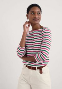 Gestreepte langemouwen shirt in groen, roze en wit; ronde hals en driekwart mouwen. Witte broek met een bruine gevlochten riem.