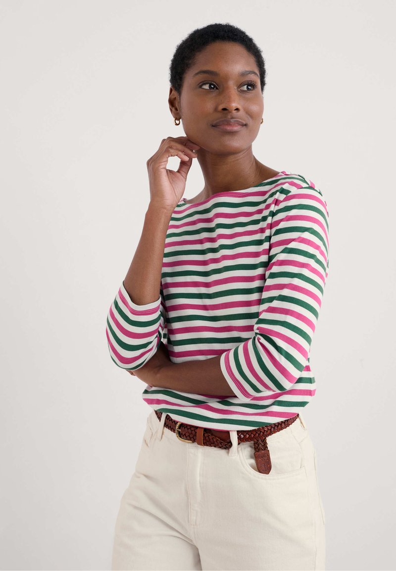 Gestreepte langemouwen shirt in groen, roze en wit; ronde hals en driekwart mouwen. Witte broek met een bruine gevlochten riem.
