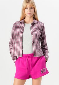 Rutig skjorta i vinröd och vit, grå t-shirt under, och ljusrosa shorts med "GAP"-logotyp, med resårmidja.