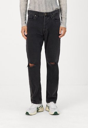 Black denim jeans with a relaxed fit, featuring two front pockets and distressed knee details. Paired with white sneakers.