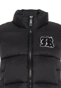 Czarna kurtka puchowa bez rękawów z wysokim kołnierzem, z zamkiem błyskawicznym z przodu i białą naszywką logo. Ma pikowaną strukturę i lekkie wypełnienie.