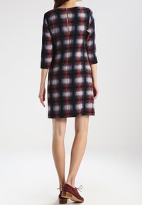 Robe longueur genoux avec un motif carreaux noir, rouge et blanc. Manches trois-quarts et fermeture éclair au dos. Assortie avec des chaussures bordeaux.