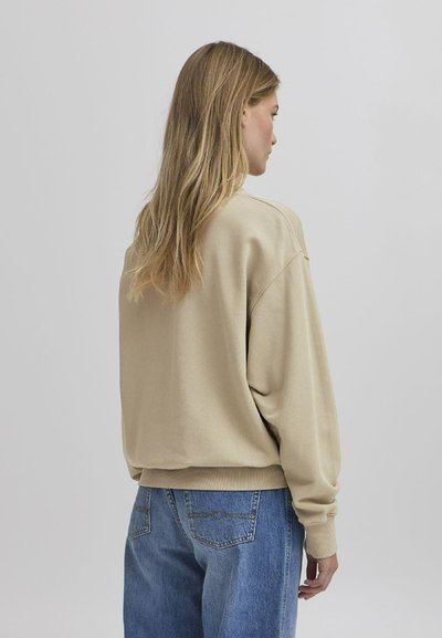 Beige bomull sweatshirt med lave skuldre og ribbede mansjetter, kombinert med lyseblå denimjeans med baklommer.