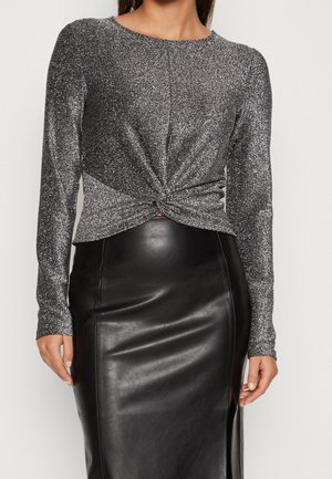Glanzend zilveren langemouwtop met een gedraaide knoopdetail aan de voorkant, gecombineerd met een zwarte faux leren kokerrok met een zijklies.