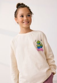Cream-colored sweatshirt made of soft fabric, featuring a playful cartoon design of three green aliens on a pink platform.