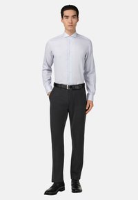 Camisa de dress de rayas azul claro con cuello abotonado, combinada con pantalones oscuros grises a medida y zapatos de cuero negros.