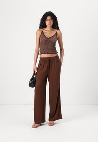 Brun ribbad crop top med justerbara remmar, tillsammans med bruna, vida byxor med elastisk midja. Accessoarer med en svart handväska.