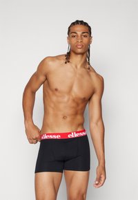 Svarta boxershorts med en röd elastisk midjeband som har "ellesse"-logotypen. Slät tyg med en figurnära design och måttlig benlängd.
