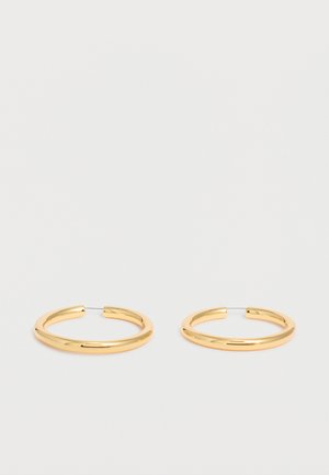 Par sjajnih zlatnih naušnica na obruč s tankim žičanim kopčama na jednobijeloj pozadini.