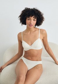 Sutien triangular cu dantelă albă și bretele ajustabile, asociat cu chiloți cu talie înaltă, amândouă fiind confecționate dintr-un material moale și elastic.