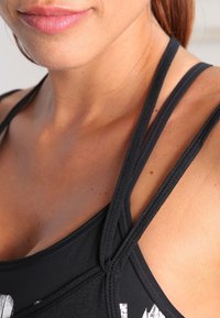 Zwarte sporttop met brede banden, voorzien van een ronde hals en textuurdetails op de stof. Soepele, elastische materialen.