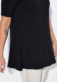 Musta lyhythihainen paita, joka on valmistettu sileästä kankaasta. Paidassa on pyöreä pääntie ja rento istuvuus, jossa on laskeutuva helma ja korostavat saumat.